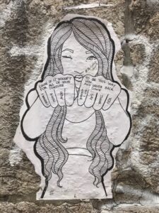 Photo of Lisbon sticker art -- a young woman with long hair is holding her fists in front of her -- written on her hands is "'Cause if it wasn't for all of your torture I wouldn't know how to be this way now and never back down so I wanna say thank you" - a part of the #shitgirlsdoproject on Instagram